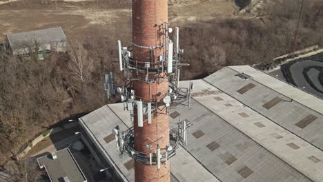 flying around of an old industrial brick chimney equipped with multiple telecommunications antennas.