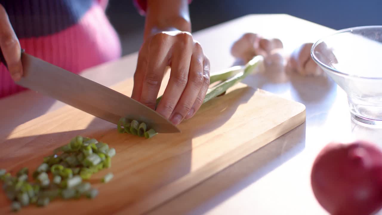 sección media de una mujer afroamericana cortando verduras en una cocina soleada