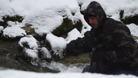 photographer in snowy forest is taking photos in a frozen creek. 4k