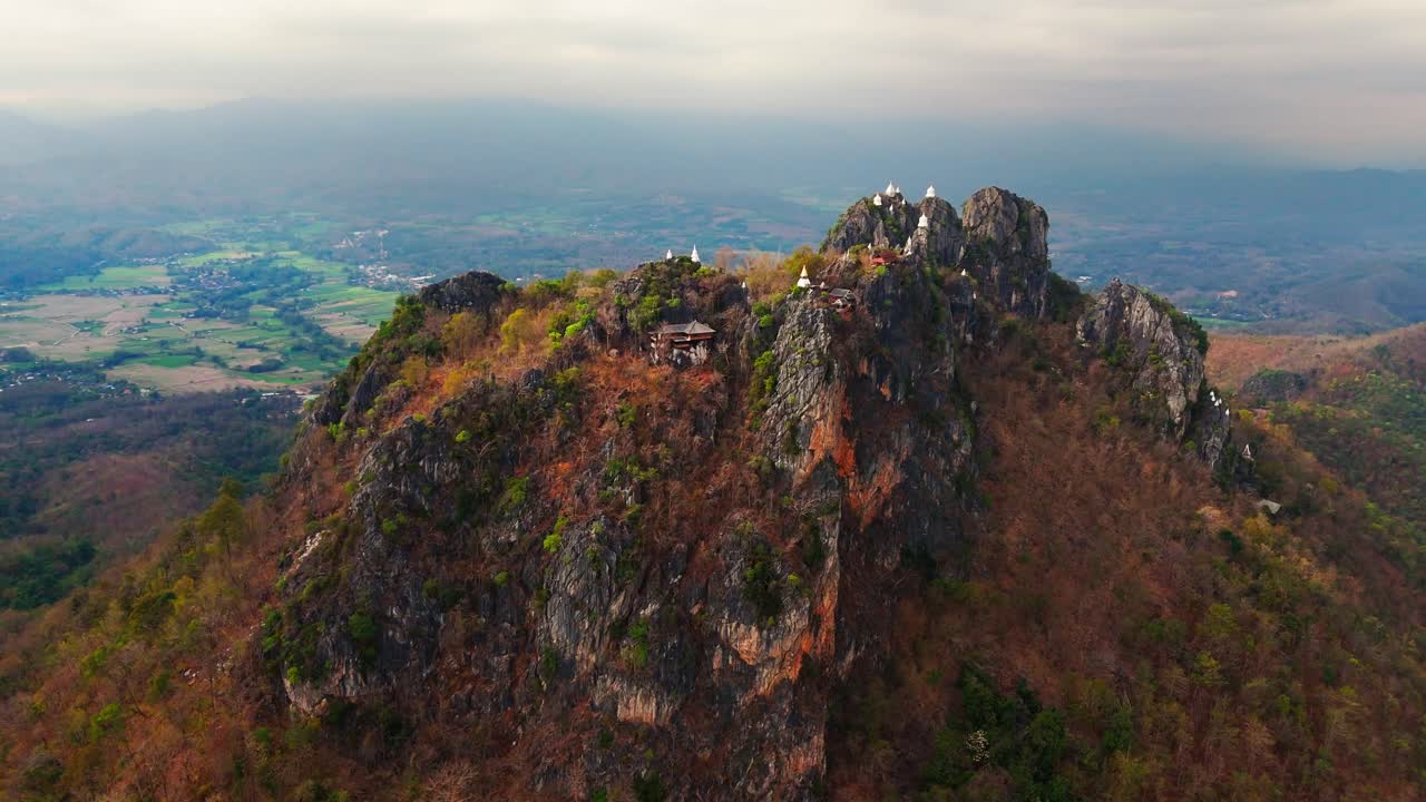 Aerial approach of mountaintop temples at Wat Chaloem Phra Kiat surrounded by dramatic cloudy sky