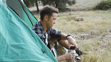 serious camping guy pouring hot drink from thermos bottle