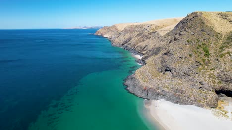 Eine-Drohnenaufnahme-Aus-Dem-Rückwärtsflug,-Die-Einen-Wunderschönen-Weißen-Sandstrand-Zeigt,-Der-Von-Hohen-Hügeln-Und-Felsformationen-Umgeben-Ist