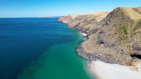 un disparo de un dron volando hacia atrás que revela una hermosa playa de arena blanca rodeada de altas colinas y formaciones rocosas