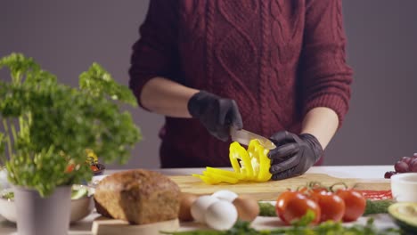 slow-motion close-up of a chef slicing a yellow bell pepper on a wooden board. black gloves ensure hygiene, while fresh ingredients like eggs, bread, and herbs create a vibrant kitchen atmosphere