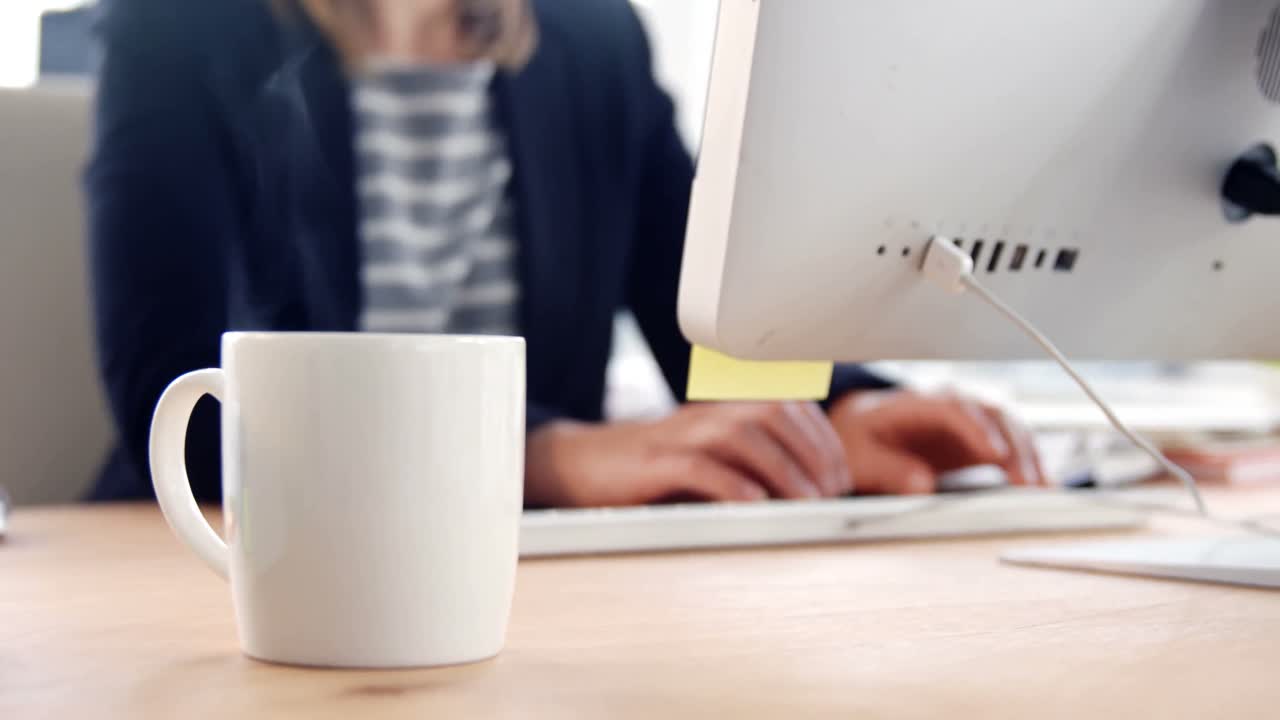 primer plano de una taza de café mientras una mujer de negocios trabaja en la computadora