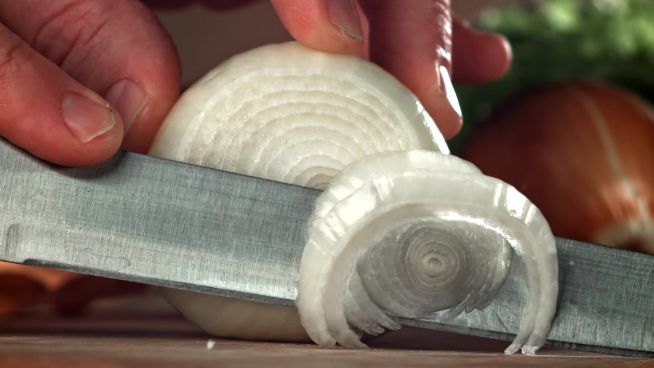 Close-up of a Hand Slicing a Fresh White Onion in Slow Motion