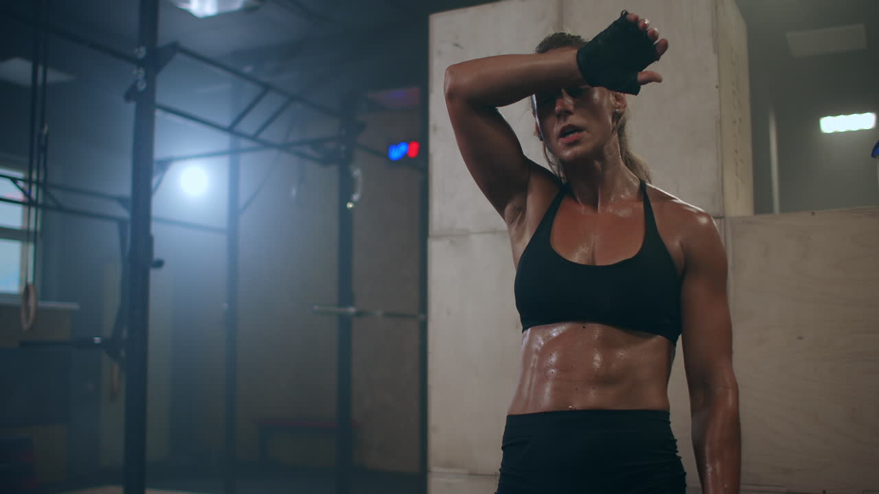 Donna fitness in salute stanca dopo un esercizio di allenamento della forza in palestra. Rallentatore: Primo piano di una modella in forma stanca che sta in piedi e si rilassa dopo un allenamento intenso.