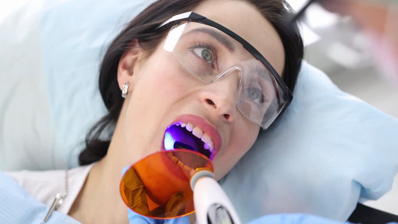 Dentist treating teeth to female patient using curing light in clinic 4k movie