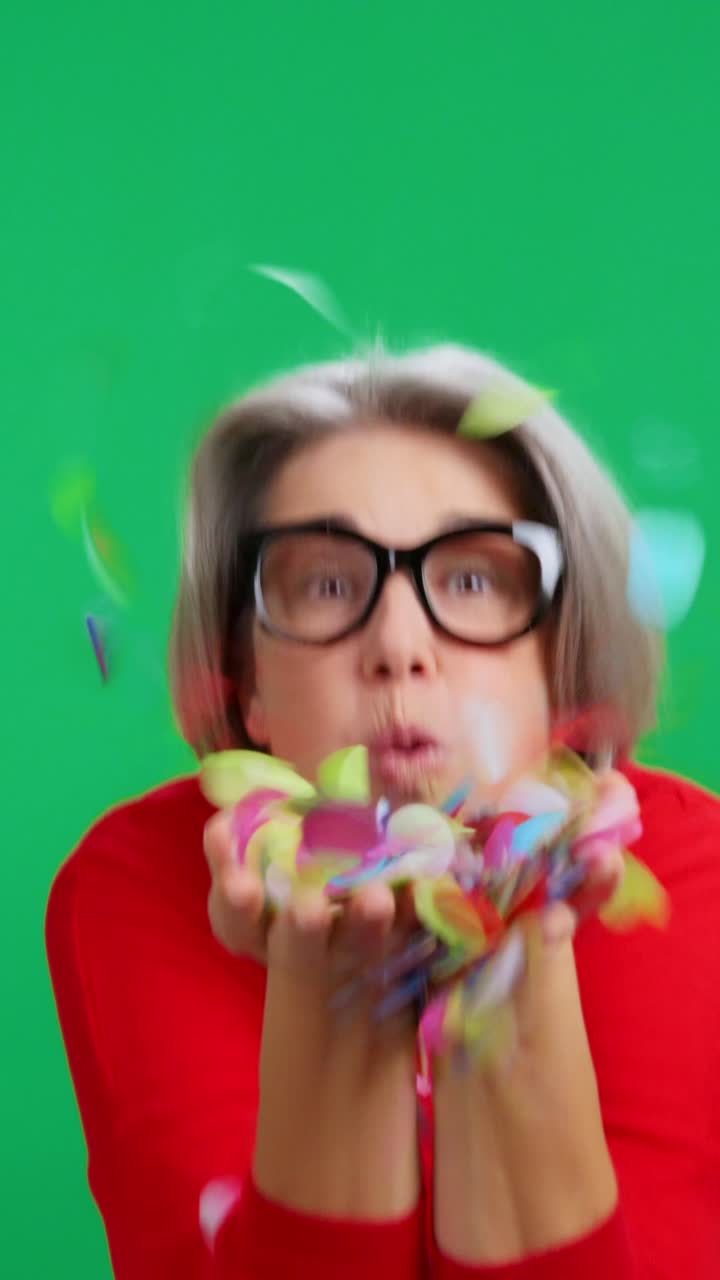 Happy Senior Woman Blowing Colorful Confetti on Green Screen