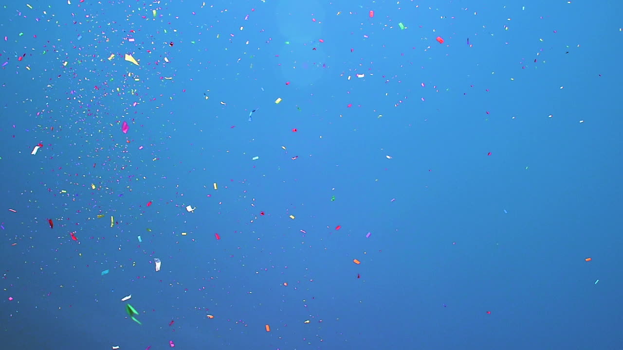 Helicopter flies through the blue skies as Confetti rains down. Summertime parade. Cinematic Slow Motion.