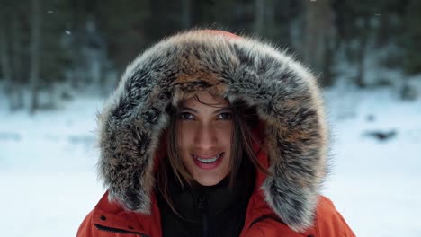 a beautiful brazilian woman in a large winter coat laughing and smiling at the camera as wind and snow passes by as she stands on a frozen lake on a cold winter day in american fork canyon, utah