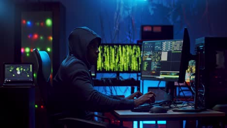 Junger-Männlicher-Hacker-In-Einer-Haube,-Der-Daten-An-Den-Beiden-Computern-Gleichzeitig-Bearbeitet-Und-Hackt,-Während-Er-Kodiert-Und-Klopft