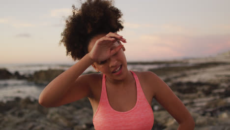 mujer afroamericana cansada de pie en las rocas cerca del mar durante la puesta del sol