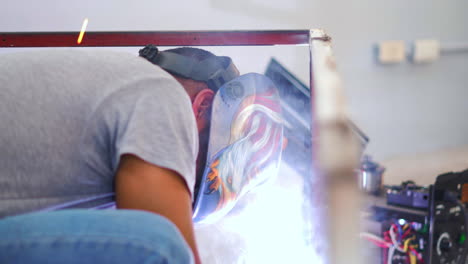 soldador experto en máscara de soldadura que fabrica marcos de acero en un taller