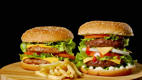 dos hamburguesas de carne artesanal en una mesa de madera aisladas en un fondo gris oscuro.