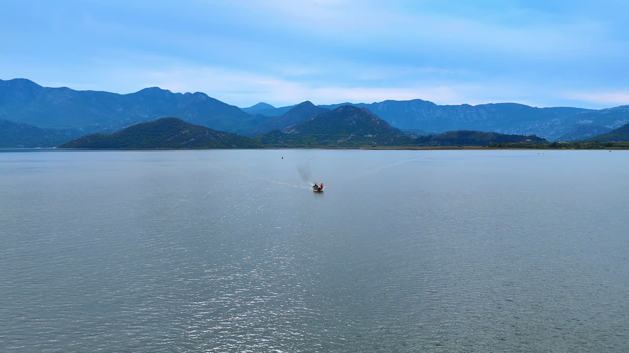 Motor boat approaches by the blue seascape. Beautiful hazy mountain ranges at the coast at backdrop. Aerial view