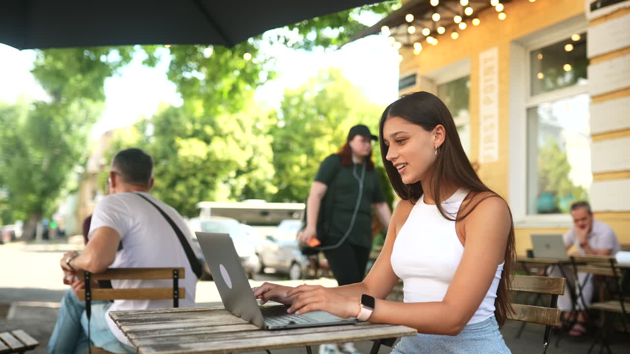 Jovem mulher trabalhando no laptop em um café ao ar livre