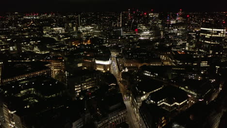 Forwards-fly-above-night-urban-district.-Tilt-down-on-cars-driving-in-streets-and-through-intersection.-Aerial-view-of-city.-London,-UK