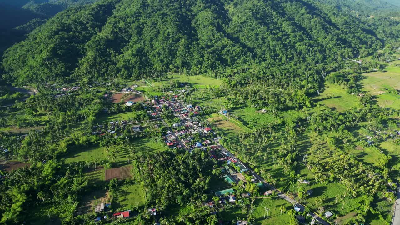 Rural barangay village town amid lush tropical greenery and mountains at Catanduanes, Philippines - aerial pullback