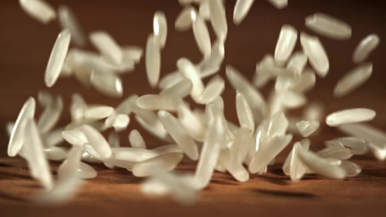 Chicchi di riso bianco che cadono al rallentatore su una superficie di legno