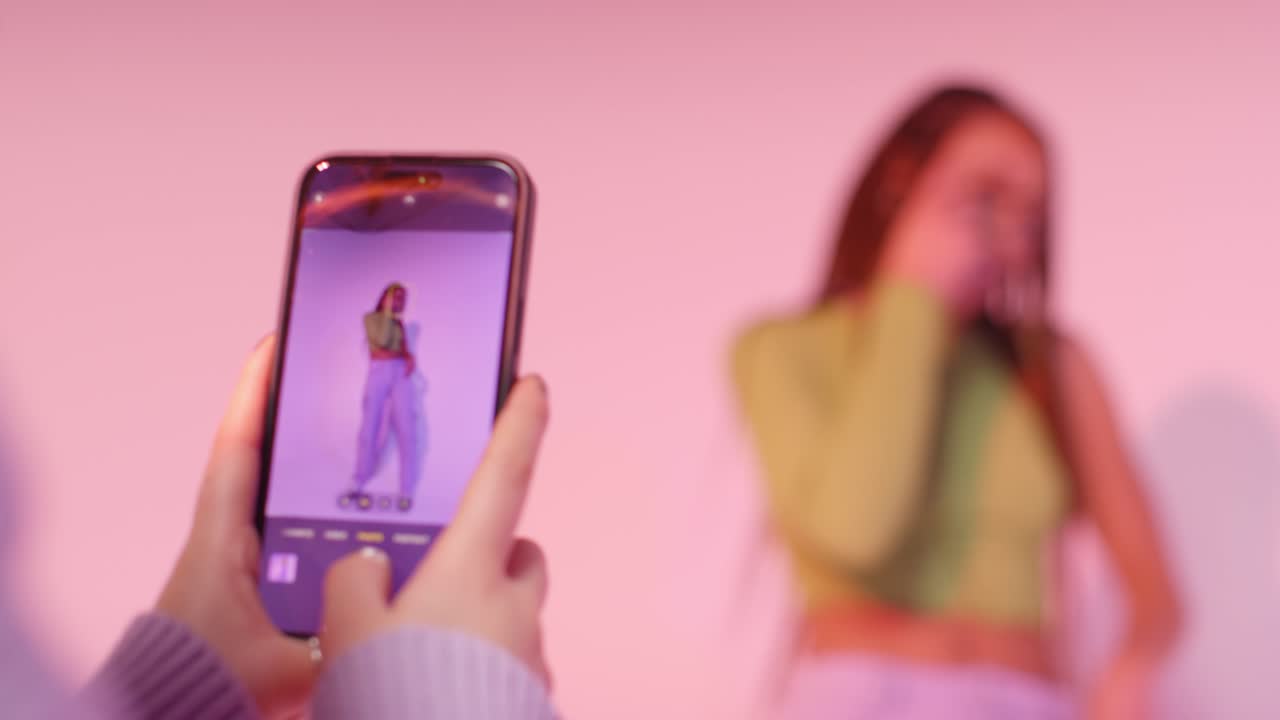fotografía de estudio de una mujer tomando una foto de una amiga bailando en un teléfono móvil contra un fondo rosa 2