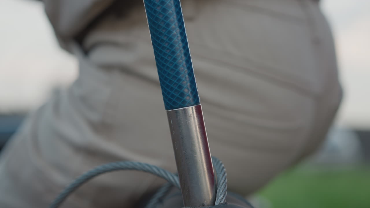 close up of person seated in wicker balloon basket securing support pole with gloved hands, inserting wooden pole into metal ferrule, coaxing rope into place under cloudy sky
