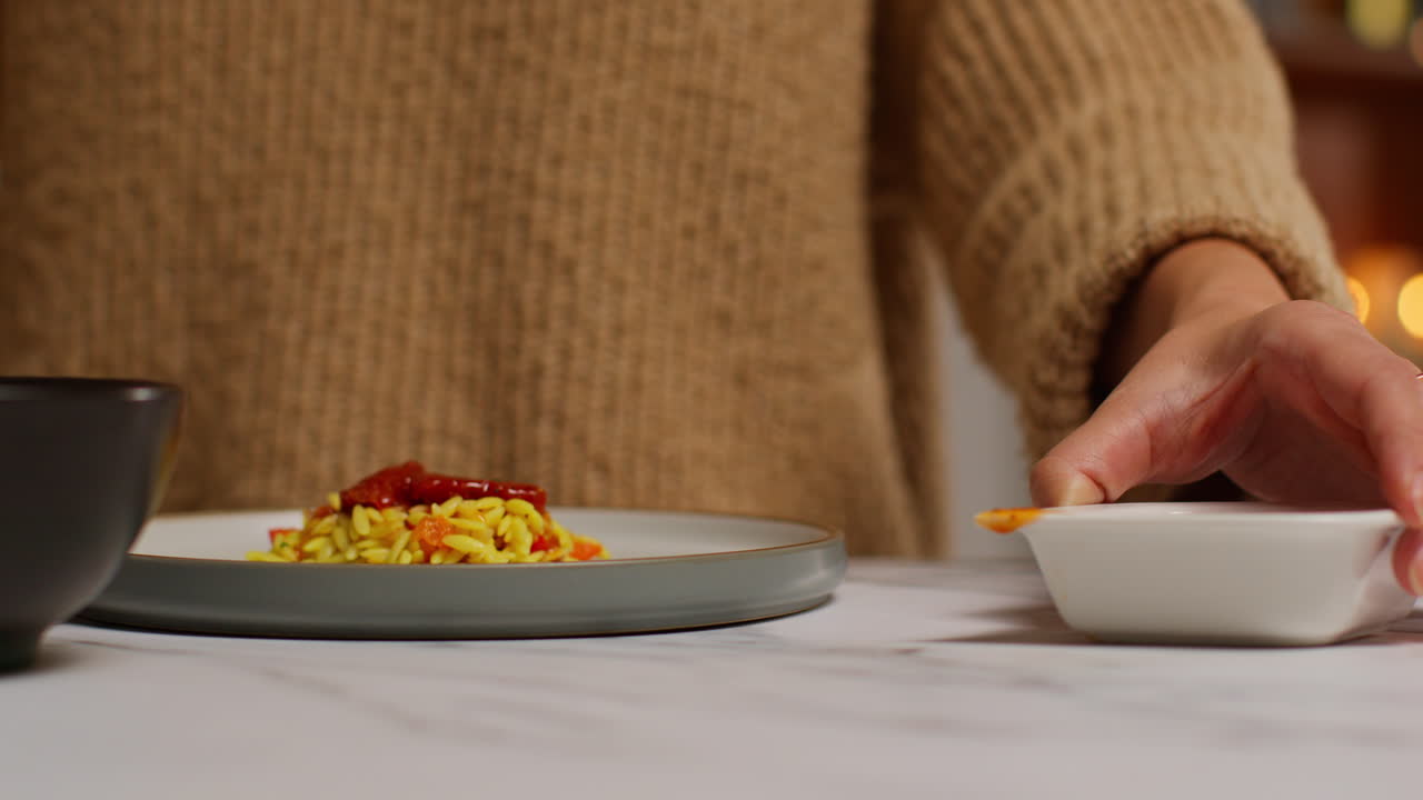 primer plano de una mujer en casa en la cocina preparando una comida saludable vegetariana o vegana vertiendo salsa sobre pasta de orzo y tomates asados 1