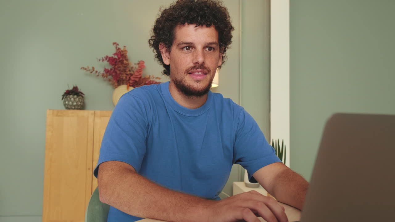 Young Man with Curly Hair Working on Laptop at Home