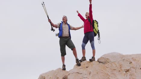 Älteres-Wanderpaar-Mit-Rucksack-Und-Trekkingstöcken-Steht-Mit-Weit-Ausgebreiteten-Armen-Auf-Den-Felsen