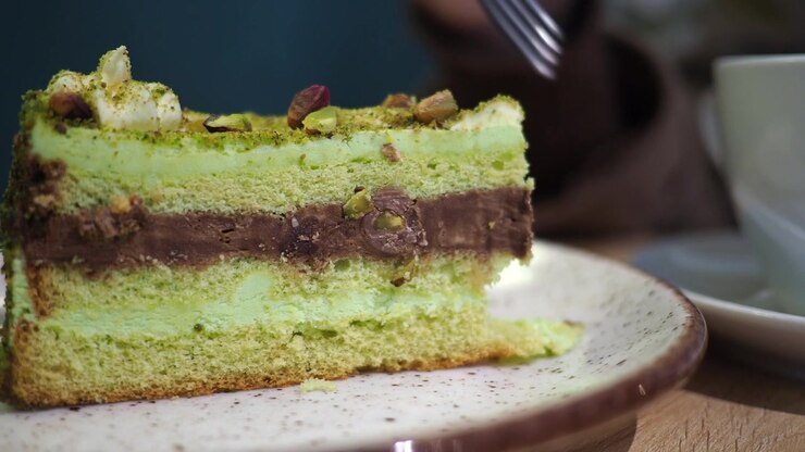 Primo piano di una forchetta che affonda in una torta a strati al pistacchio e cioccolato