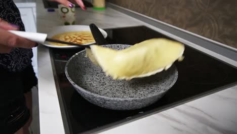 a female hand with spatula pushes pancake around a pan and turning it around. homemade pancakes. slow motion shot