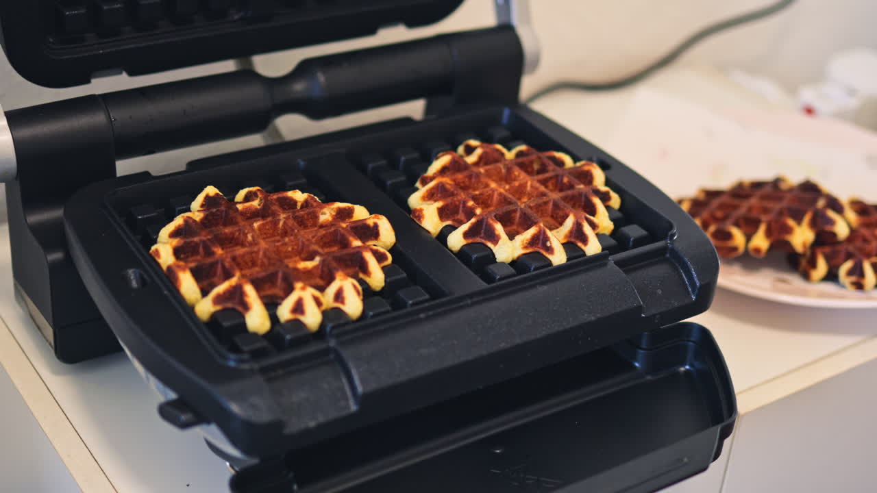 Waffles doces são preparados em uma grelha elétrica. Uma máquina de waffles onde waffles crocantes são preparados.