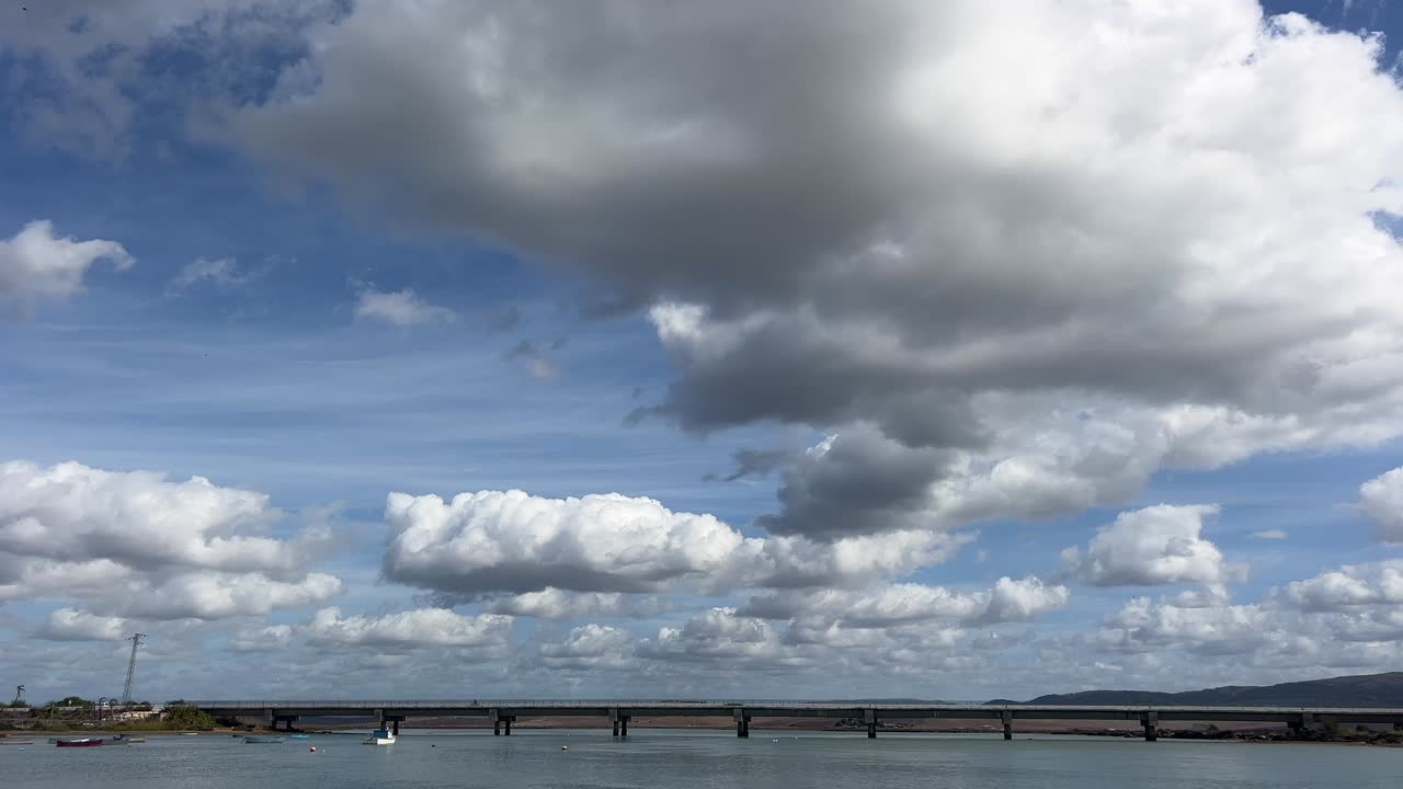 View of clouds moving over the sea and a bridge. Daylight. Time lapse