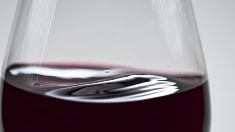 merlot wine lightly shaking glass closeup. grape rose beverage surface waving