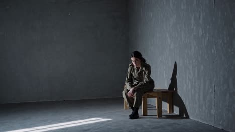 young female soldier is sitting alone on a wooden bench in a dark room, her head bowed and her body slumped, conveying a sense of sadness, isolation, and despair