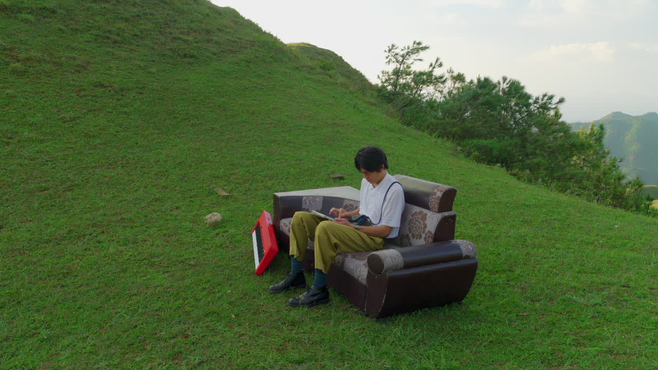 artist sitting on a couch outside use a tablet for writing a new song with his red piano keyboard
