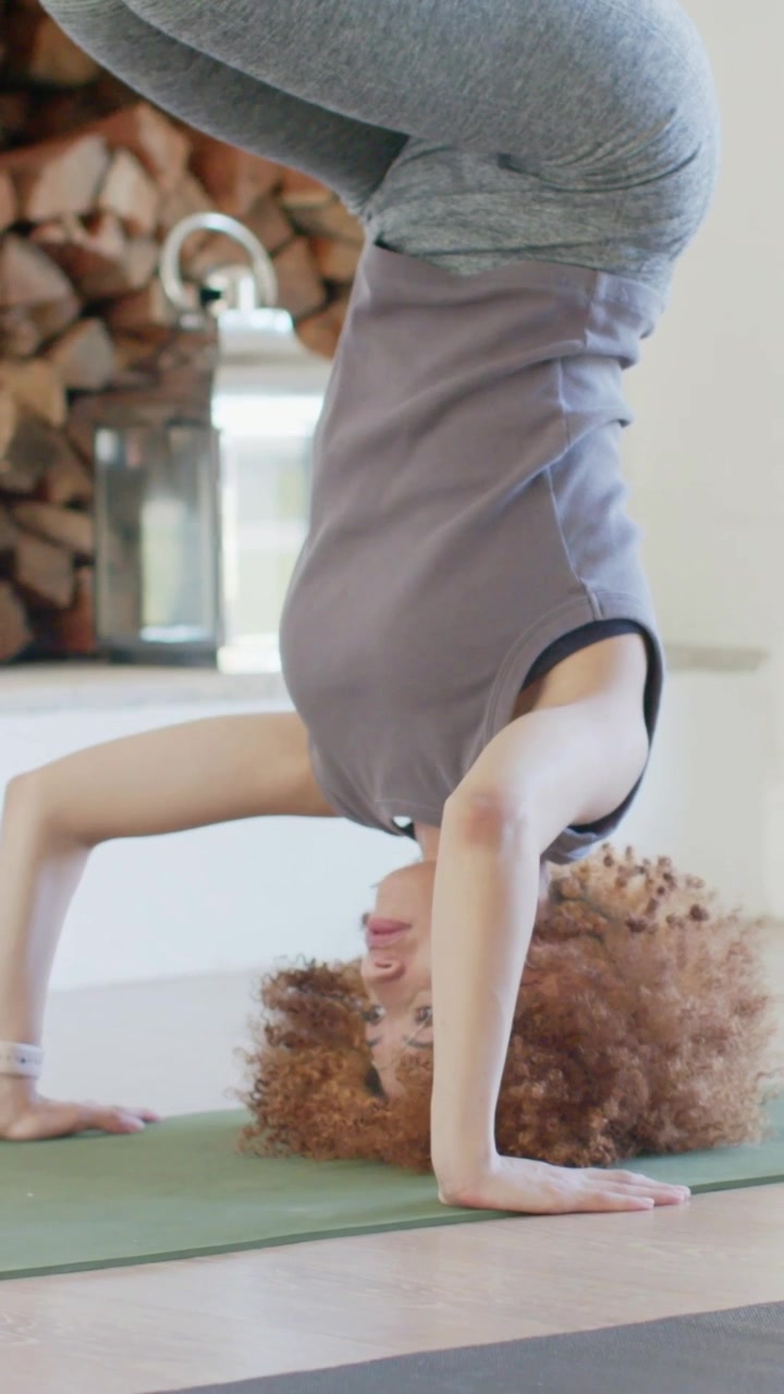Video verticale: Donna in leggings che si sistema e mantiene una posizione sulla testa su un tappetino verde a casa per l'equilibrio