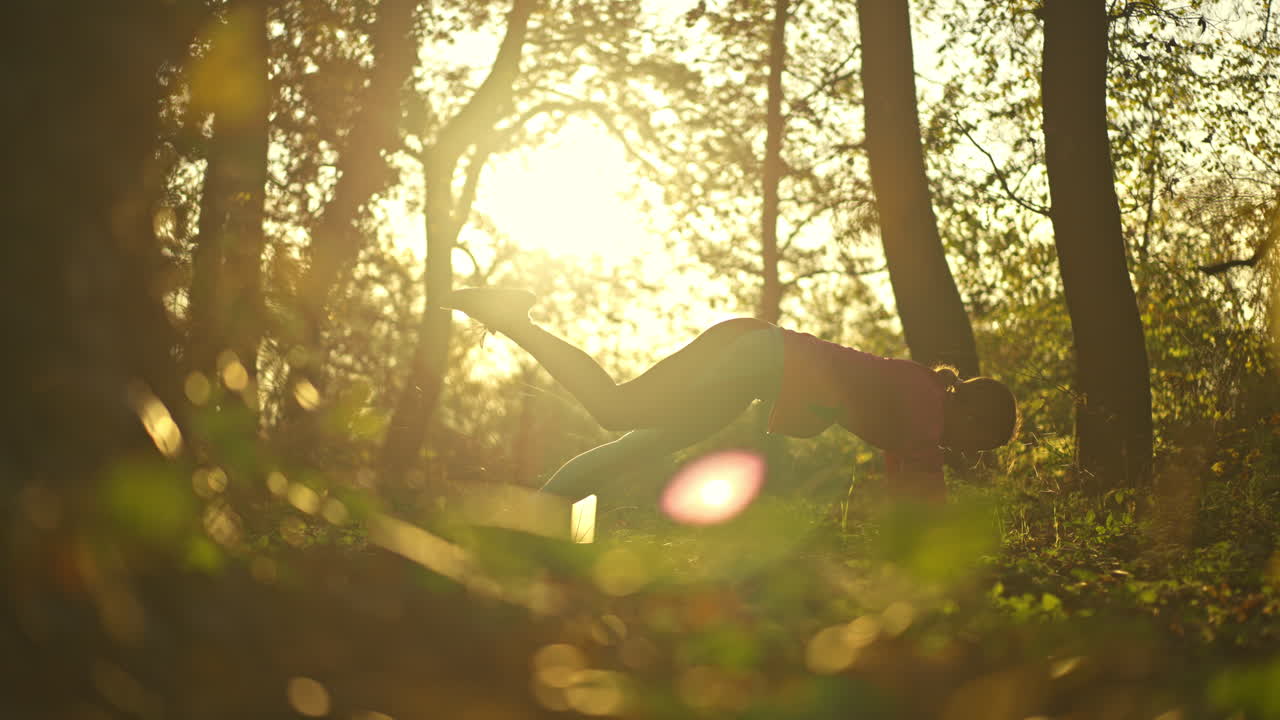 Woman practicing yoga in a serene forest at golden hour