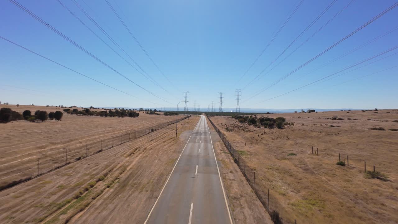 drone flying forward and rising above a empty paved road with high power lines on each side in a dry hot landscape in Australia