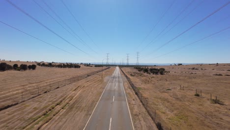 drone flying forward and rising above a empty paved road with high power lines on each side in a dry hot landscape in australia