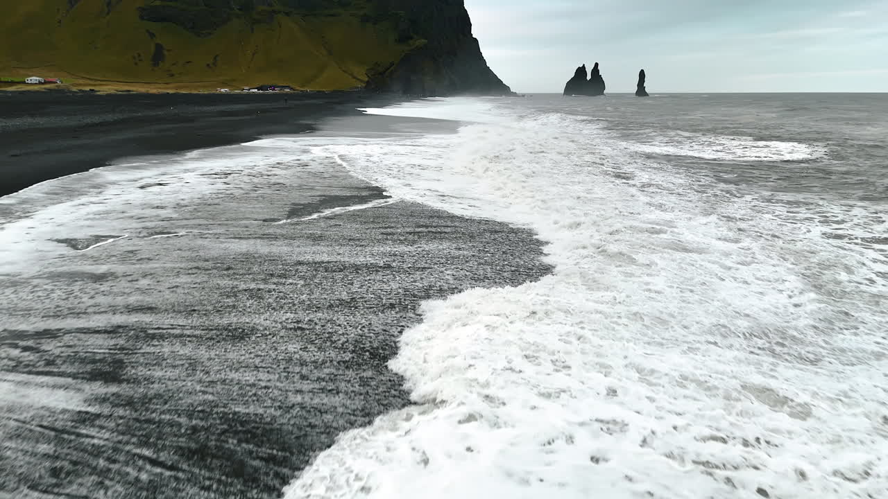 Stormy weather at the coastline. Strong white foamy waves roll on the black beach. Shoreline of Iceland.