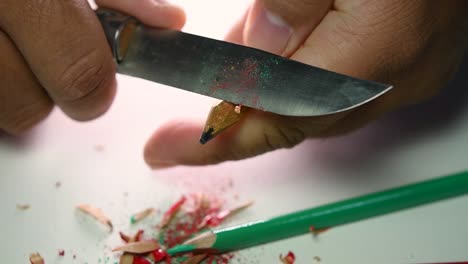 imágenes de manos afilando lentamente un lápiz y algunos lápices de colores con un cuchillo afilado