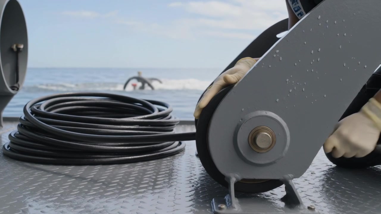 Surface splash signaling ROV recovery, gloved crew member guiding tether through stern pulley