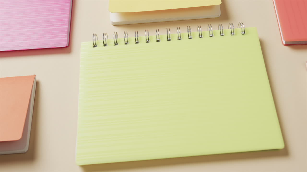 Close up of colourful notebooks arranged on beige background, in slow motion