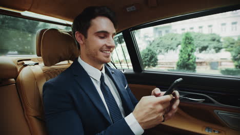 un hombre de negocios alegre escribiendo un mensaje en su teléfono inteligente en un coche de lujo.