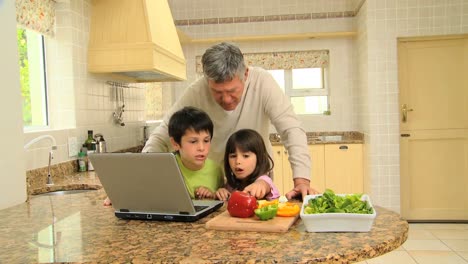 man and his grandchildren following a recipe on a laptop