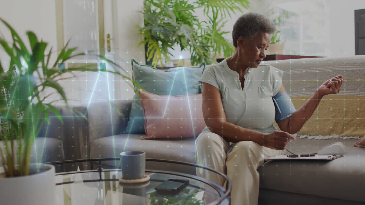 Animation of cardiograph over senior biracial woman taking pressure at home