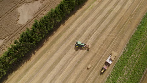 A-Farm-Tractor-In-A-Field-Carrying-A-Square-Bale-Of-Hay-Loading-It-To-A-Trailer-For-Transport