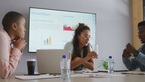 Three-diverse-creative-male-and-female-colleagues-in-discussion-at-meeting-using-laptop-and-screen