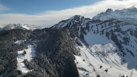 Panorámica-Aérea-Sobre-Montañas-Cubiertas-De-Nieve-Y-Bosques-De-Pinos,-Largas-Sombras-Proyectadas-Desde-La-Cresta-En-El-Día-Del-Cielo-Azul